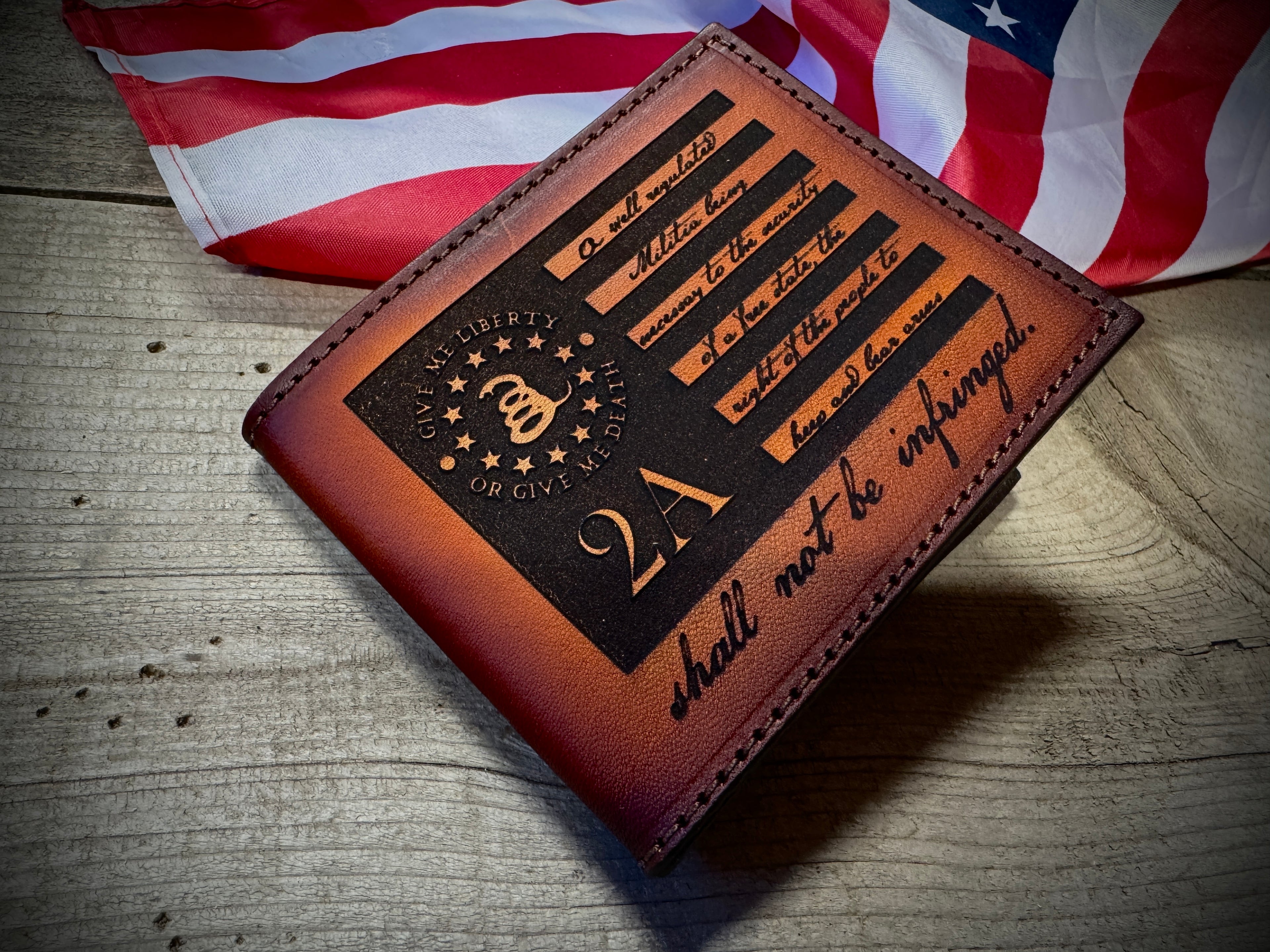 Brown leather wallet with Second Amendment Laser engraved text and design on a wooden surface with an American flag in the background - made in USA