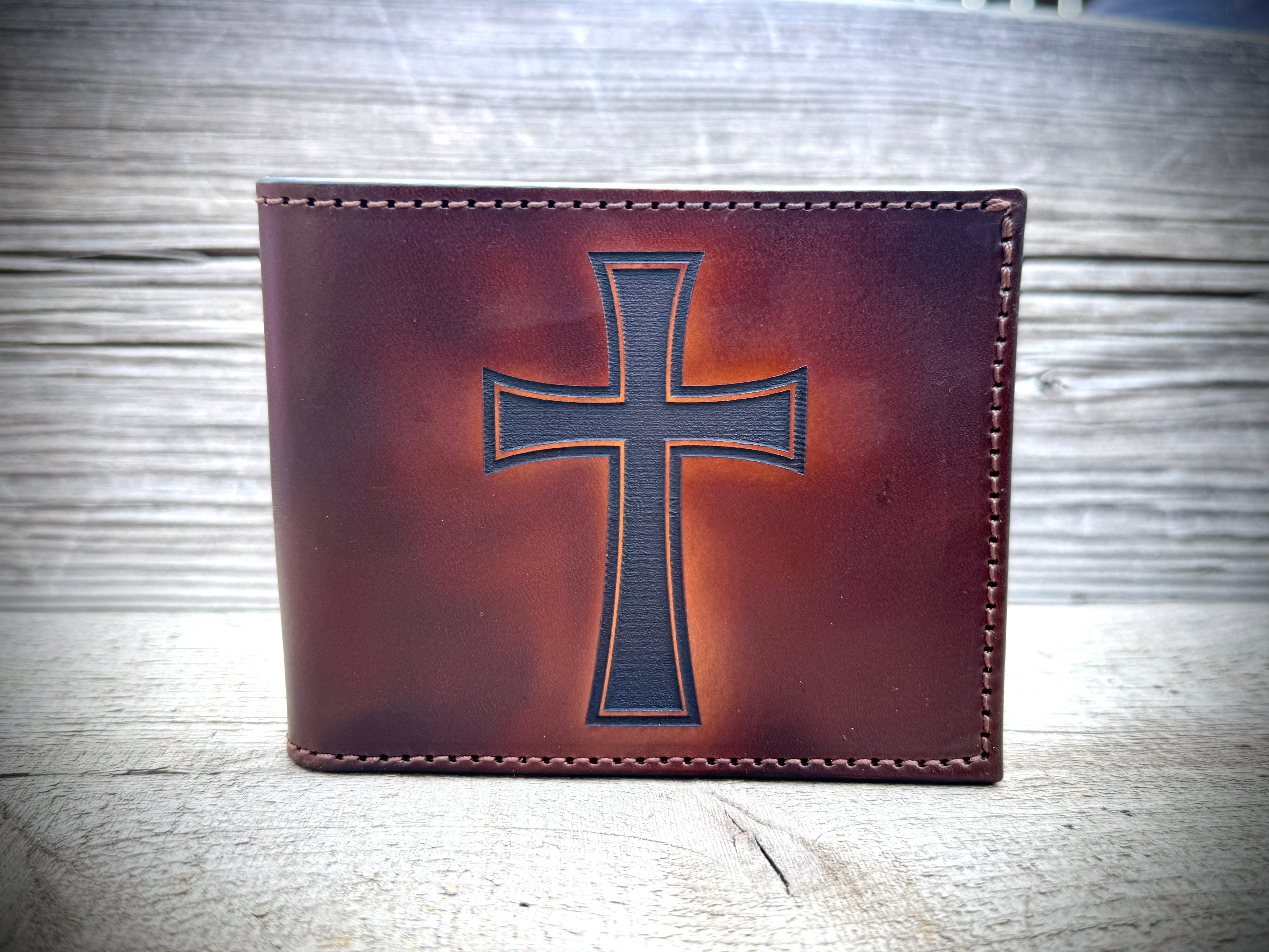 Brown leather wallet with a cross design on a wooden surface