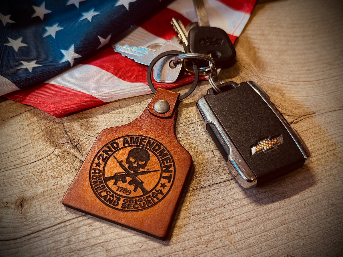 Keychain with '2nd Amendment' design on a wooden surface with an American flag in the background.