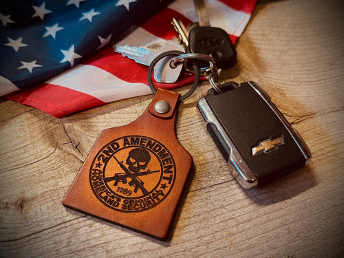 Keychain with '2nd Amendment' design on a wooden surface with an American flag in the background.