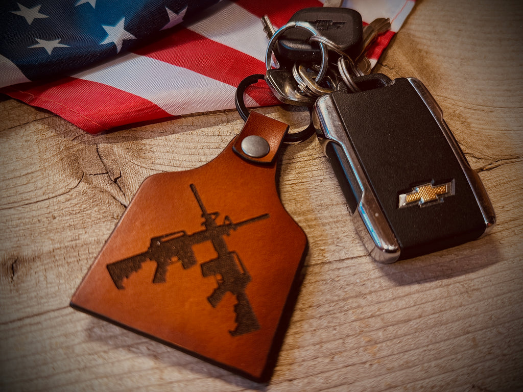 Keychain with rifle design on leather tag and multi-tool on wooden surface with American flag in background