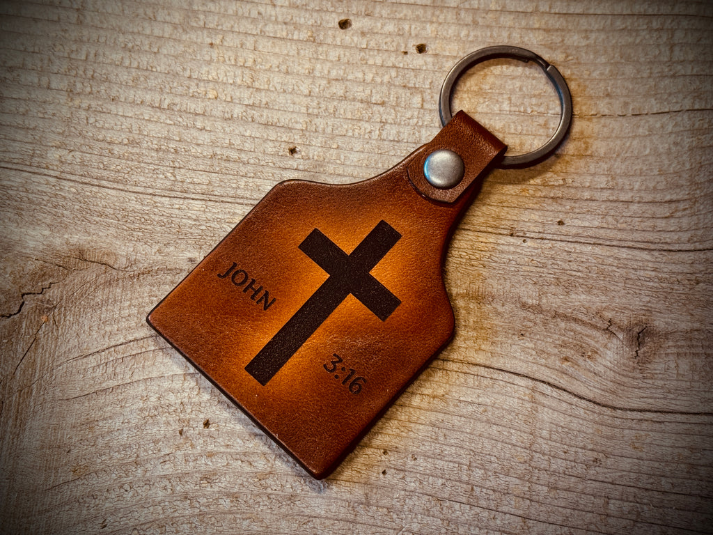 John Brown leather keychain with cross and text on a wooden surface:16 