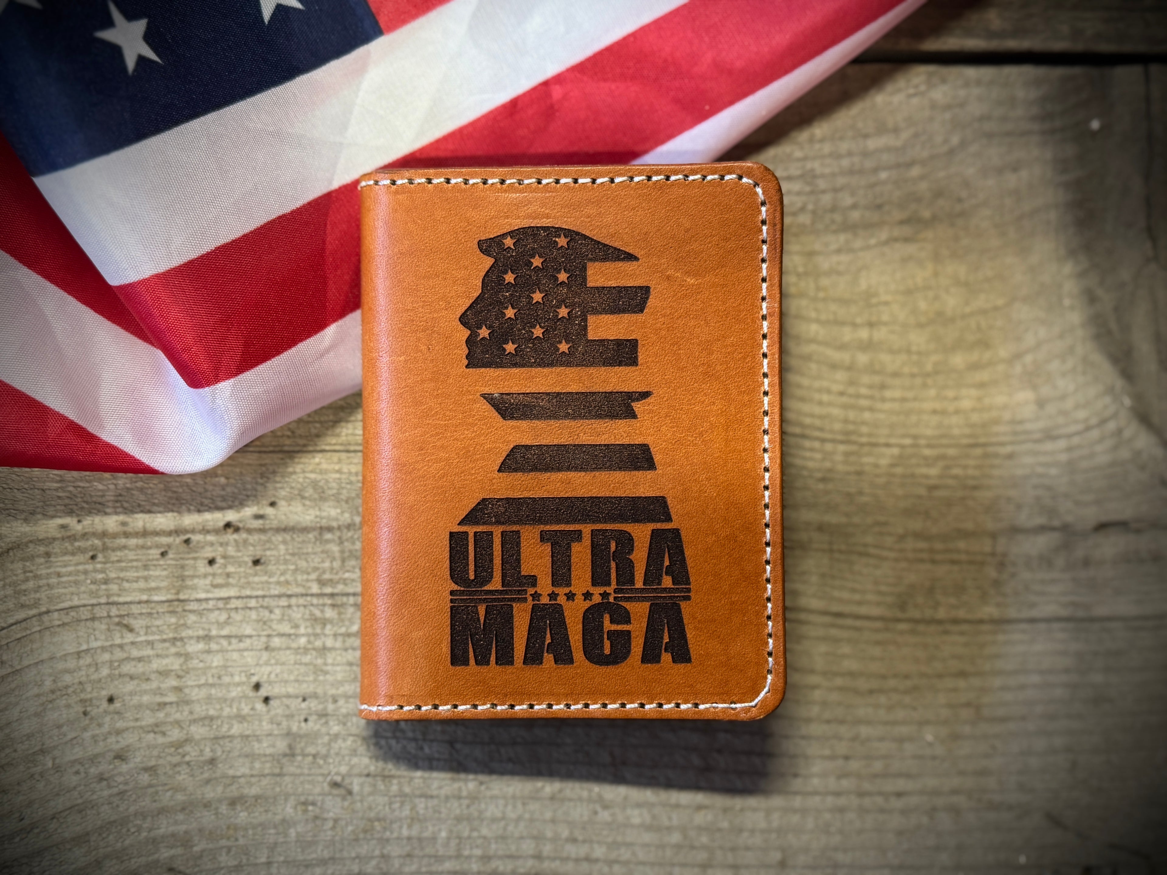 Brown leather credit card wallet with 'ULTRA MAGA' engraving on a wooden surface with an American flag in the background.