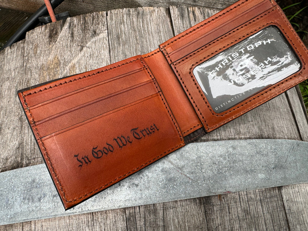 Brown leather wallet with 'In God We Trust' engraving on a wooden surface